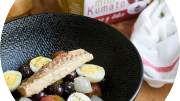 Plato negro con ensalada de tomate y huevos de codorniz; bolsa de tomates al fondo.